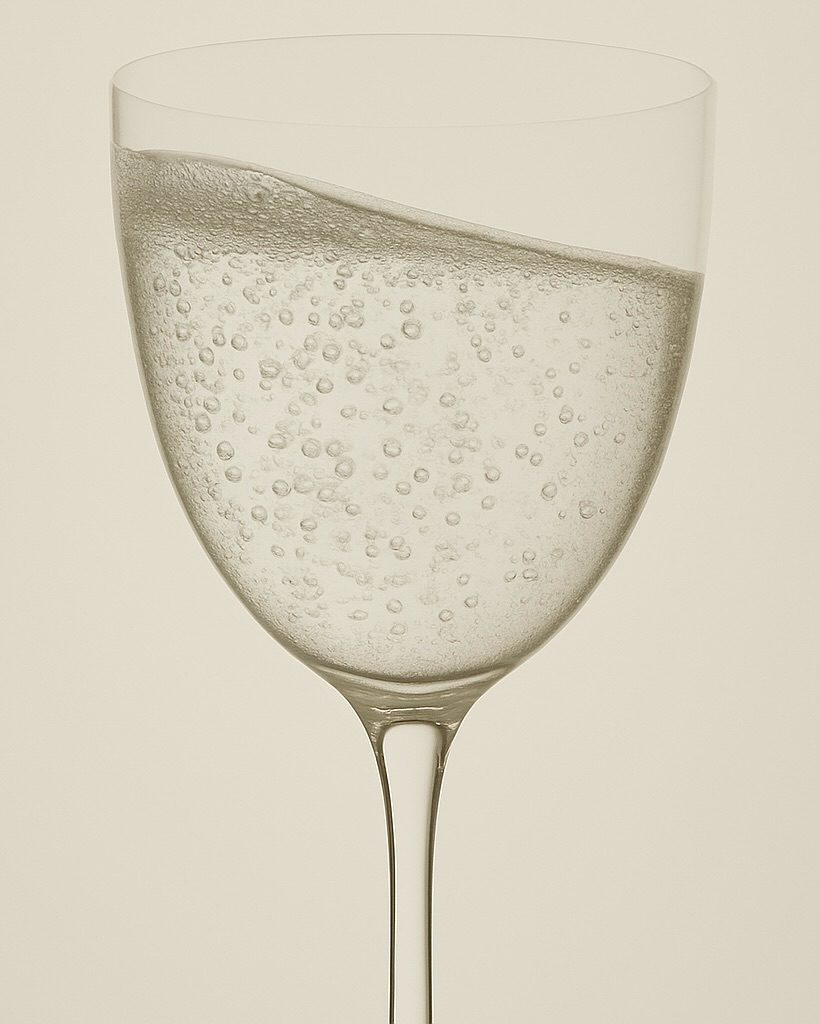 A stemmed glass of Astra, carbonation rising through pale liquid.